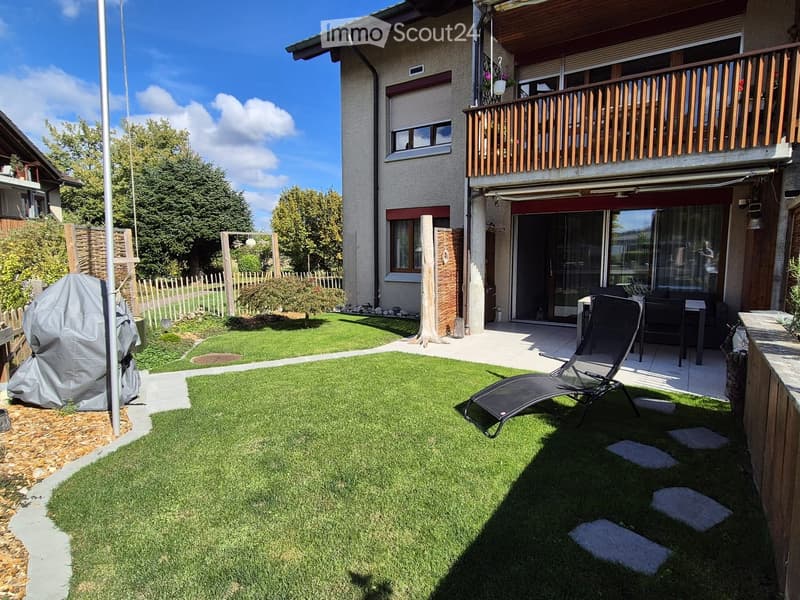 Well-maintained garden with green lawn, patio area, covered barbecue, and outdoor furniture including a lounge chair and table.