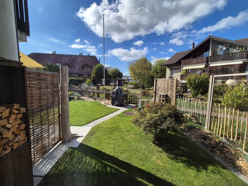 Well-maintained garden with a neatly trimmed lawn, wooden fences, a stack of firewood, and surrounding residential houses.