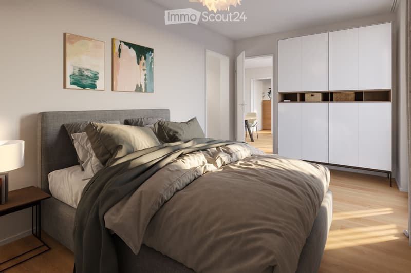 Modern bedroom with a grey upholstered bed, nightstand, lamp, and white built-in cabinet. Two abstract paintings adorn the wall, and the room features light wooden flooring.