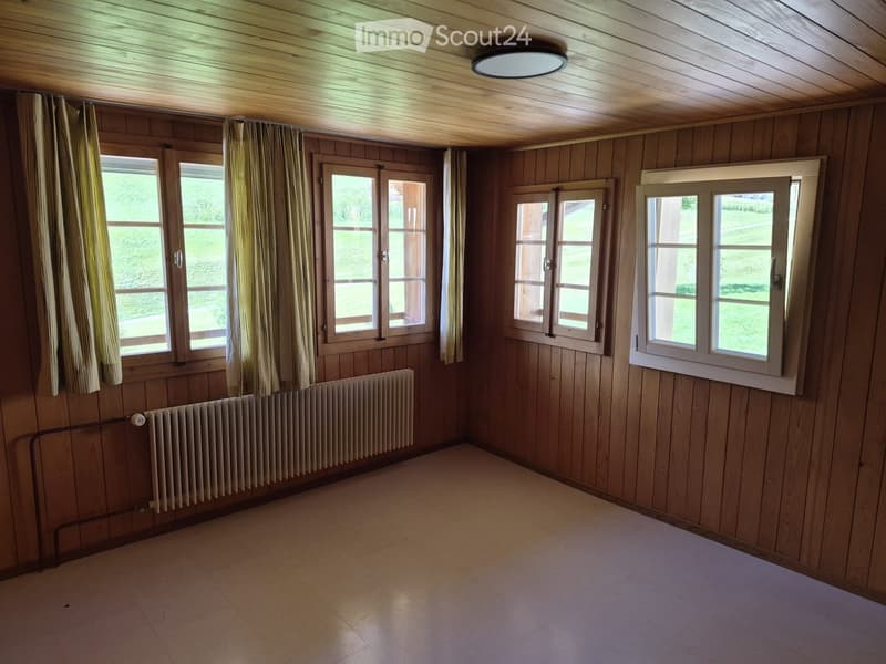 Empty room with wooden walls, tiled floor, multiple windows with curtains, and a radiator.