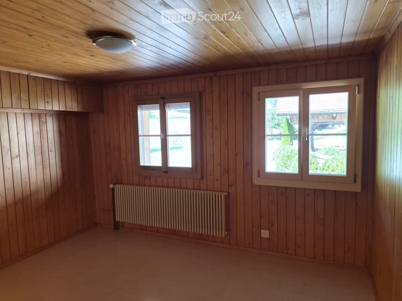 Empty room with wooden walls, wooden ceiling, two windows, and a radiator.