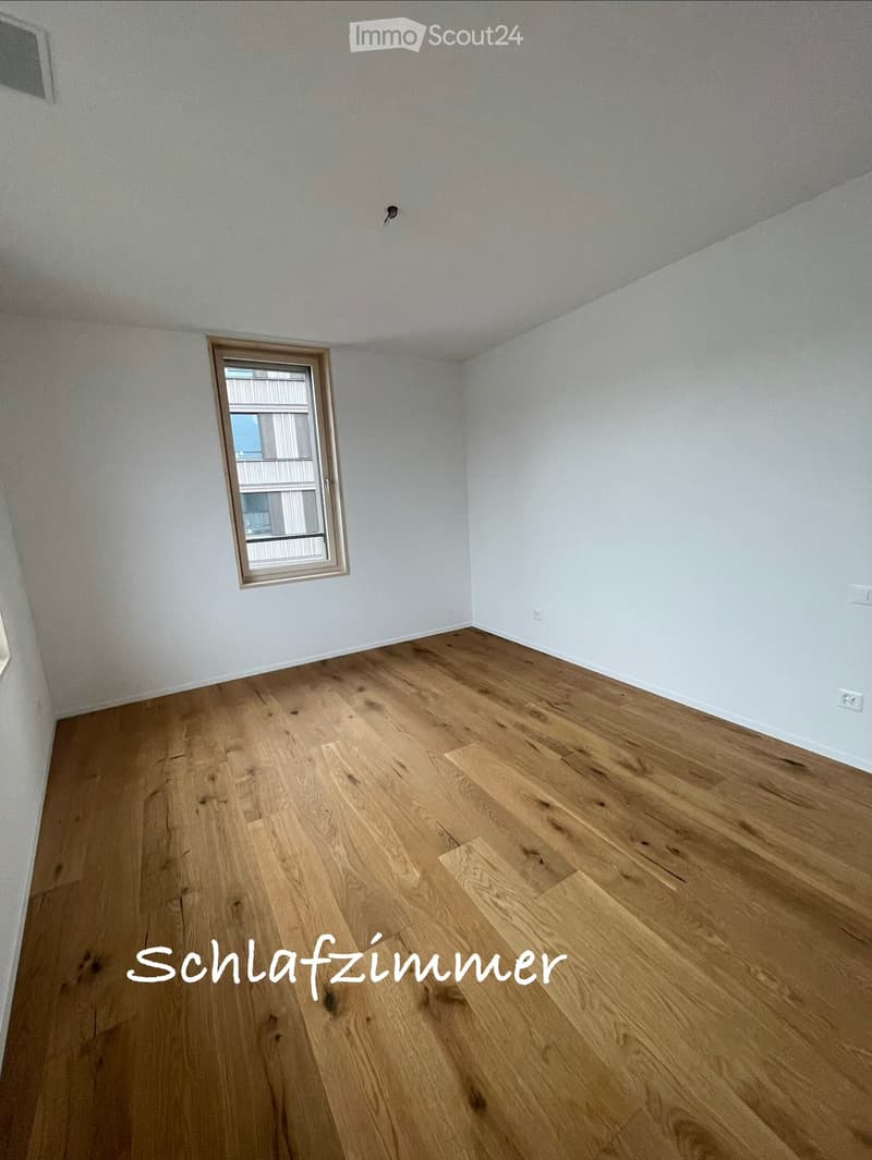 Empty room with light wooden flooring and white walls, featuring a single window with a view of an adjacent building.