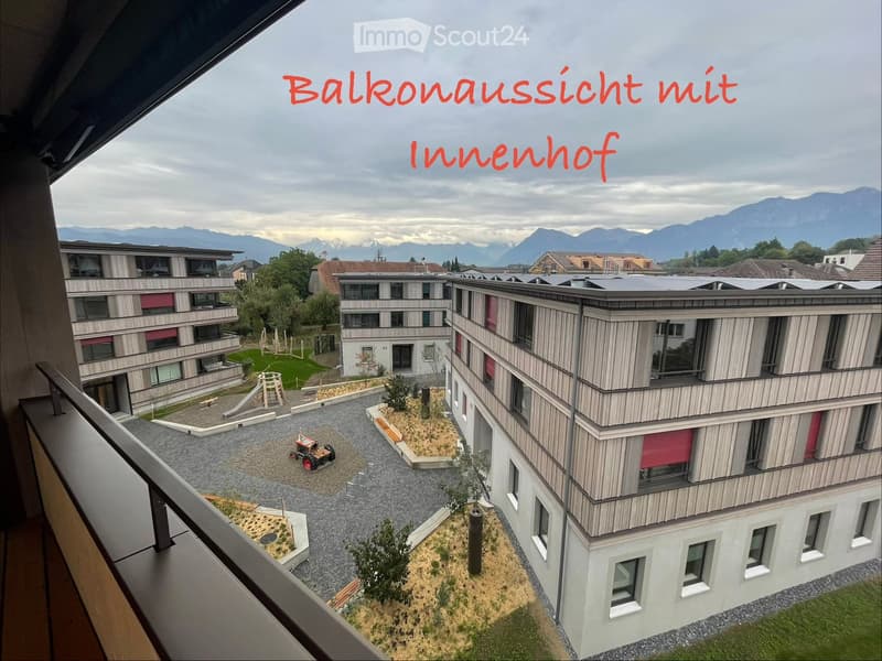 Balcony view showing a modern residential complex with a landscaped inner courtyard, playground, and surrounding mountains.
