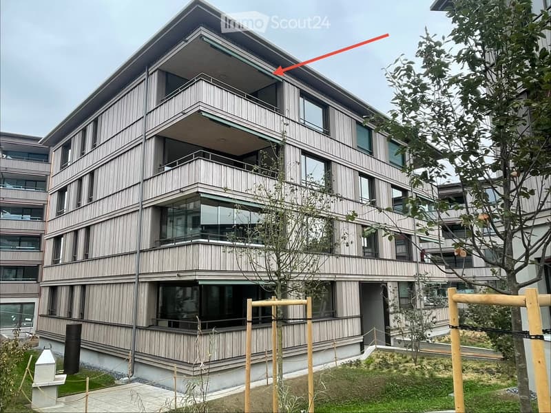 Modern multi-story building with wooden siding, large windows, and balconies. The structure features a contemporary design with clean lines and a raised ground floor.