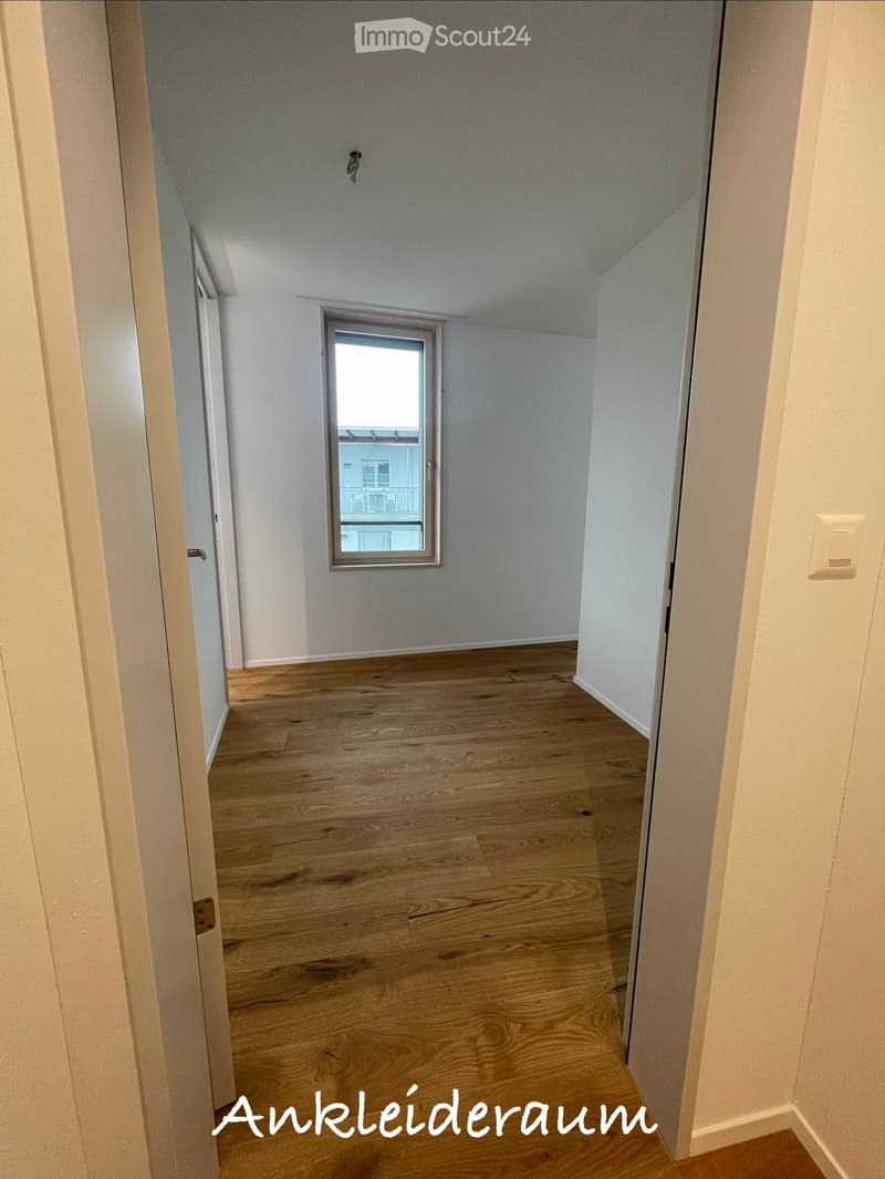 Empty hallway with wooden flooring, white walls, and a small window at the end.