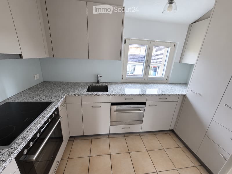 Modern kitchen with white cabinets, granite countertop, built-in oven, sink, and tiled floor.