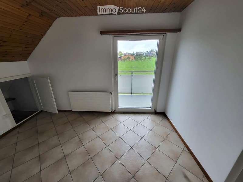 Empty room with tiled floor, white walls, wooden ceiling, and a large window with a view of a green area.