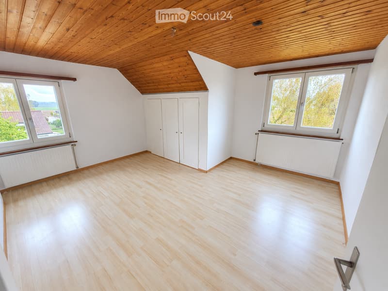 Empty attic room with wooden flooring, white walls, and skylight windows. Features built-in closet doors and radiators.