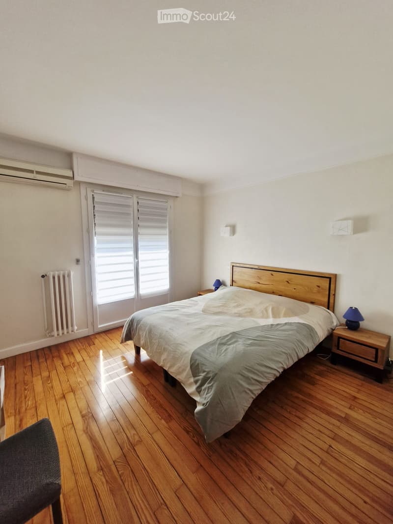 Cozy bedroom with wooden flooring, a double bed with a wooden headboard, nightstands with lamps, and a radiator near the window.