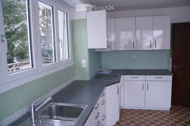 Modern kitchen with white cabinets, dark countertops, and a stainless steel sink. The walls are painted in a light blue color with green tiles along the lower half. The floor has a checkered pattern.
