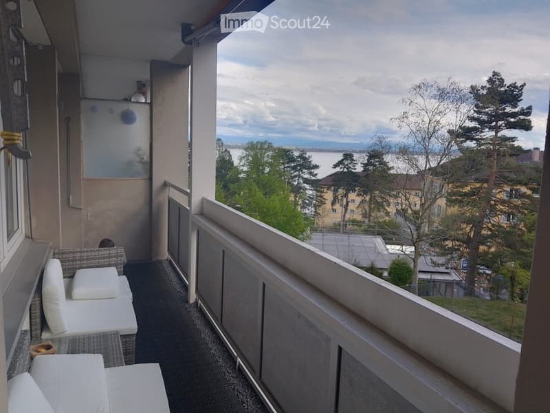 Balcony with white cushions, a small table, and a scenic view of a lake and surrounding trees.