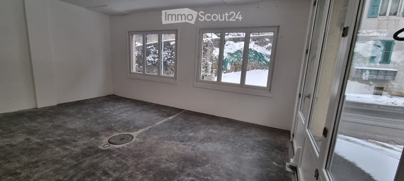 Empty room with bare walls, concrete floor, and large windows overlooking a snowy outdoor area.