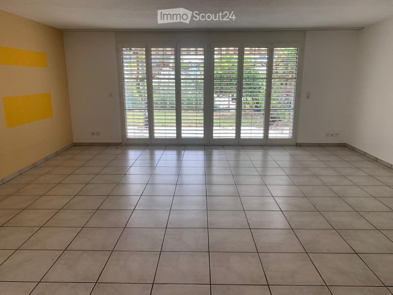 Empty room with tiled floor, large sliding glass doors with blinds, and neutral-colored walls.