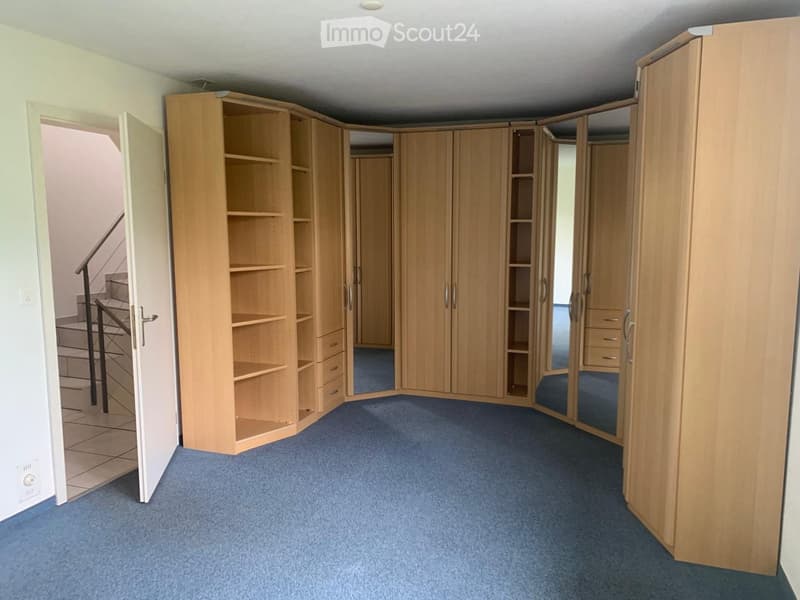 Empty room with light wooden built-in wardrobes and shelves, blue carpeted floor, and an open doorway leading to a staircase.