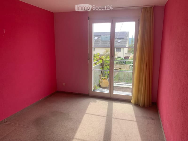 Empty room with pink walls, carpeted floor, large sliding glass door leading to a balcony, and yellow curtain on one side.