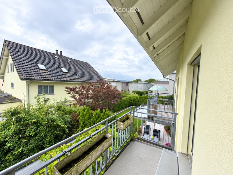 Balcony with metal railing, small wooden planters, and a view of a garden and neighboring houses.
