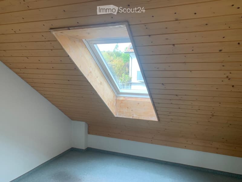 Empty room with wooden slatted ceiling, skylight window, and grey carpeted floor.