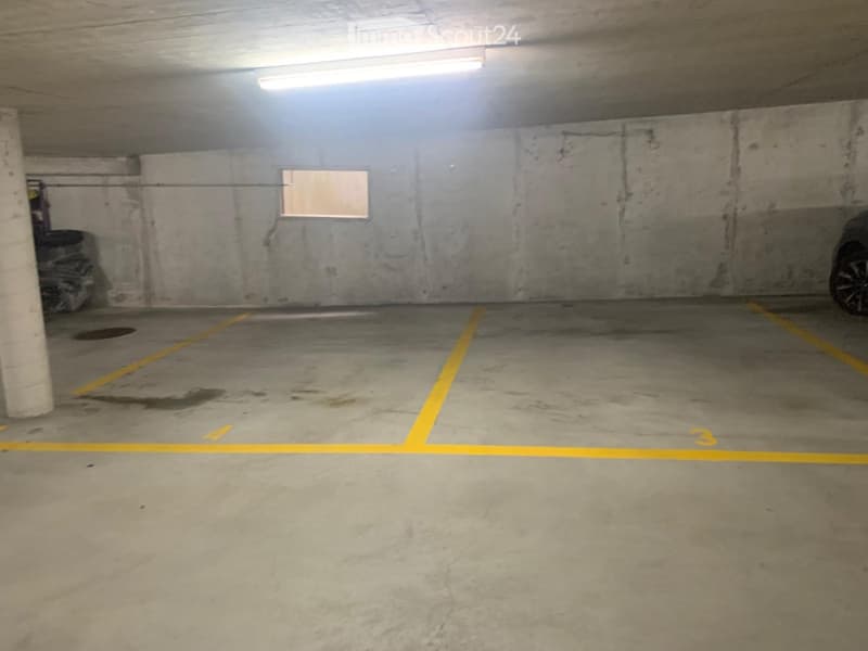 Empty underground parking space with concrete walls, floor markings, and a single car partially visible on the right side.