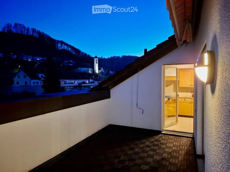 Balcony with tiled floor, open sliding door leading to a brightly lit kitchen with yellow cabinets.