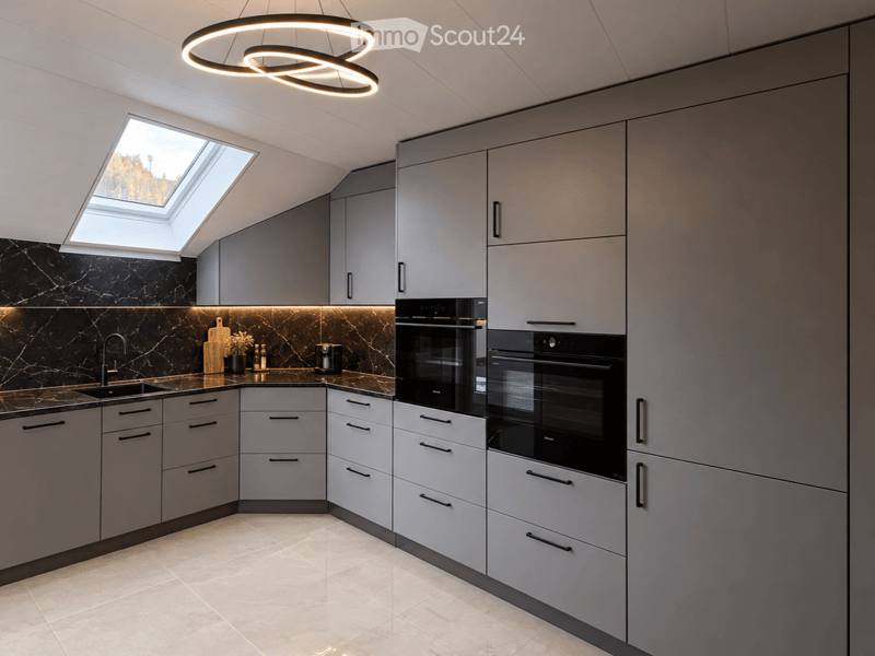 Modern kitchen with grey cabinets, black marble backsplash, and built-in ovens. Features a circular light fixture, a skylight, and a sink with a faucet.