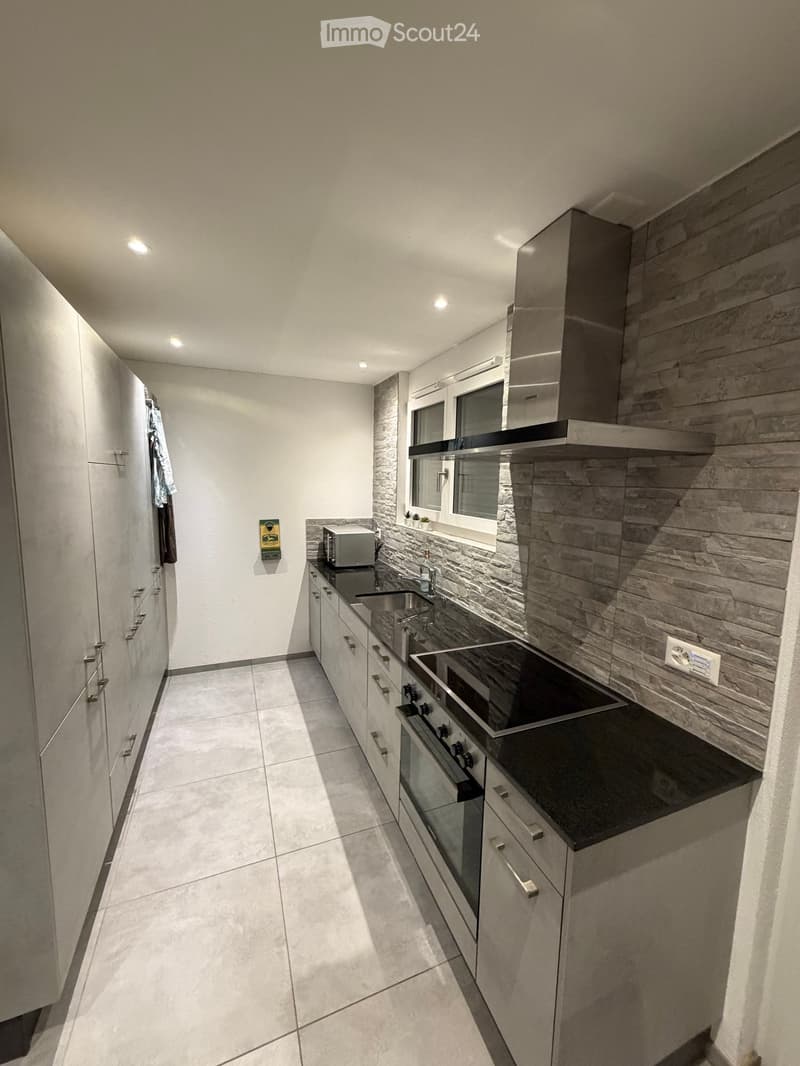Modern kitchen with white cabinets, stainless steel appliances, and a stone backsplash.