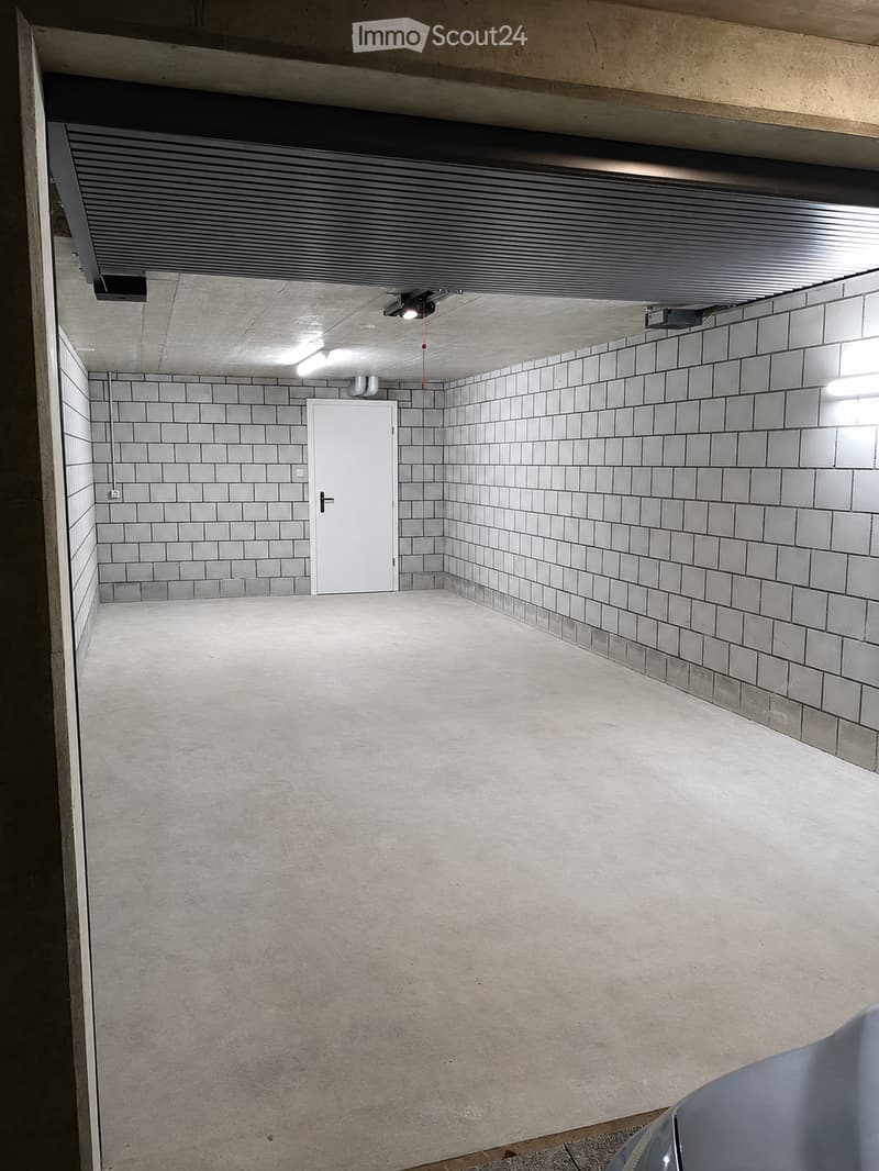 Empty underground parking space with concrete floors, tiled walls, and a single white door.
