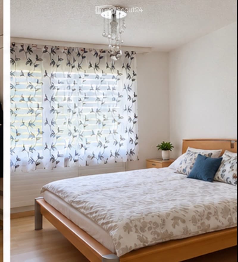 Cozy bedroom with a wooden bed, patterned bedding, nightstand, potted plant, and a decorative chandelier.