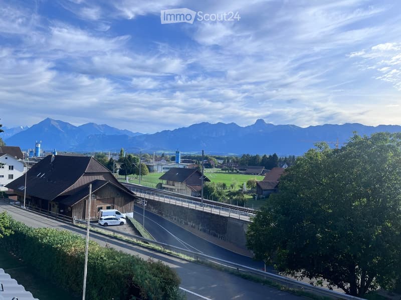 A rural village scene with a wooden barn, a road, and distant mountains under a partly cloudy sky.