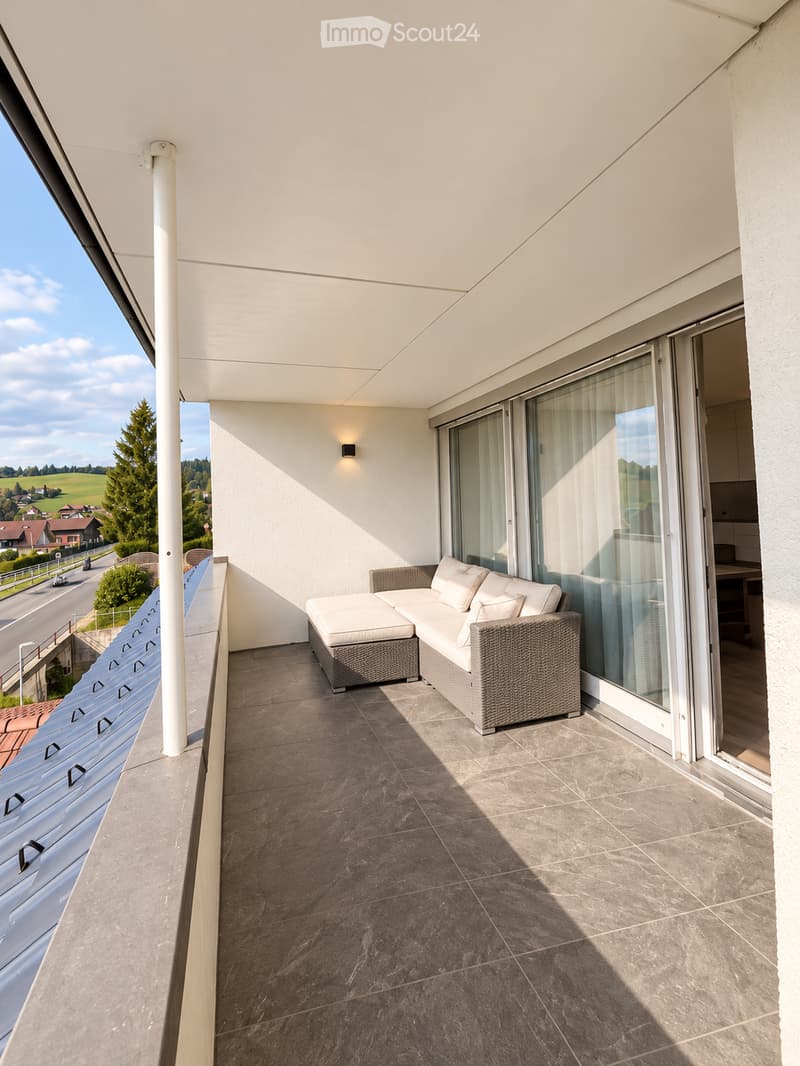Balcony with a modern white sofa, large windows, and a scenic view of the countryside.