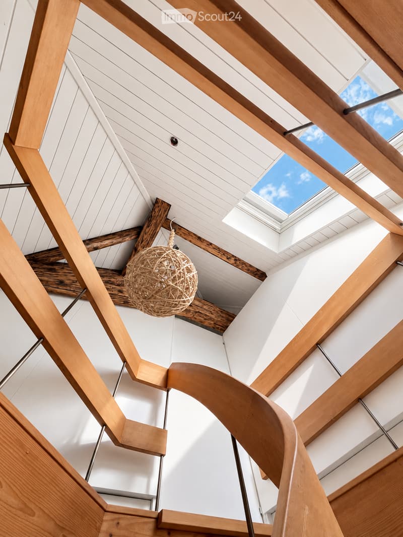 Modern interior with exposed wooden beams, white paneled ceiling, and a hanging woven light fixture.