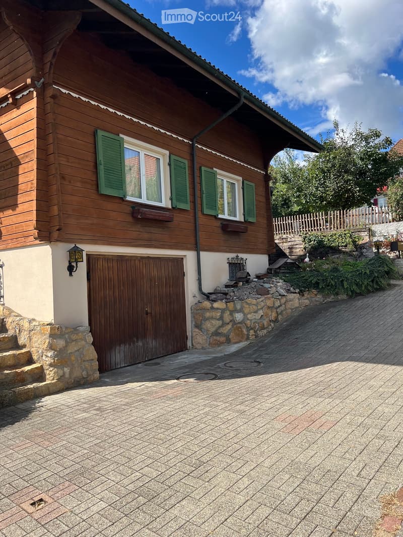 Two-story wooden house with green shutters, a garage, and a stone pathway leading to the entrance.
