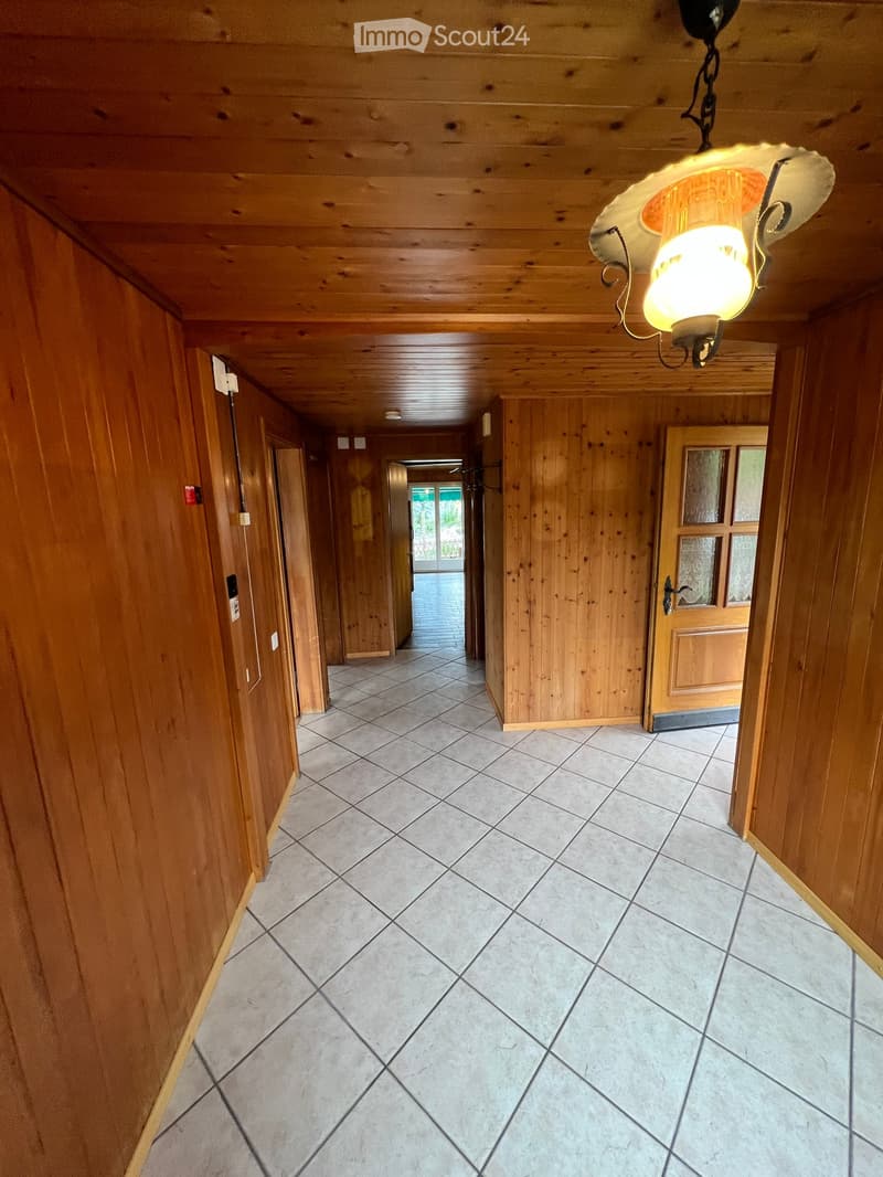 Wooden-paneled hallway with tiled floor, wooden doors, and a hanging light fixture.