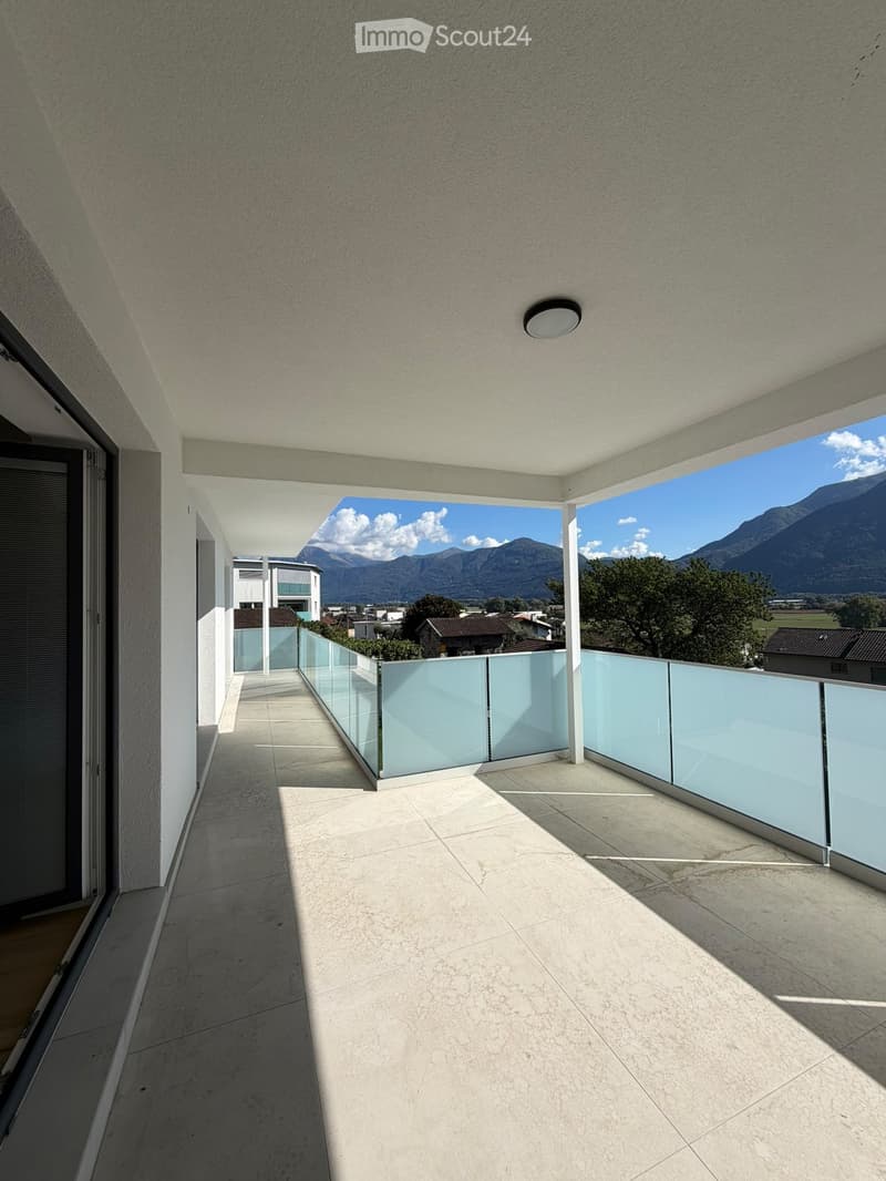 Modern balcony with light-colored tiled flooring, glass railings, and a scenic mountain view in the background.