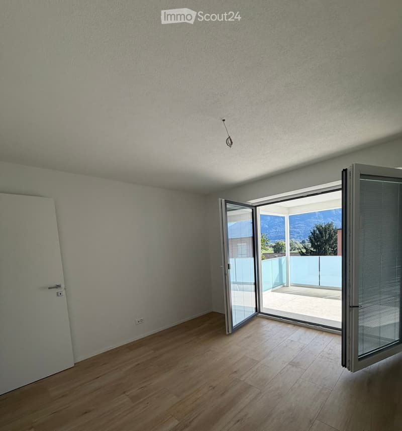 Empty room with light-colored wooden flooring, white walls, and large sliding glass doors leading to a balcony with a scenic mountain view.