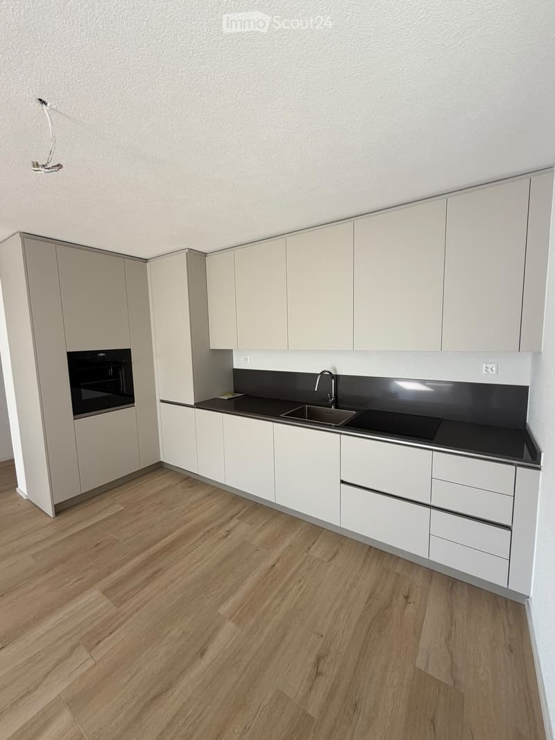 Modern kitchen with white cabinets, wooden flooring, and a black countertop featuring a sink and oven.