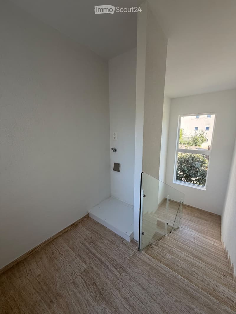 Modern bathroom with a glass-enclosed shower stall, light wooden flooring, and a window providing natural light.