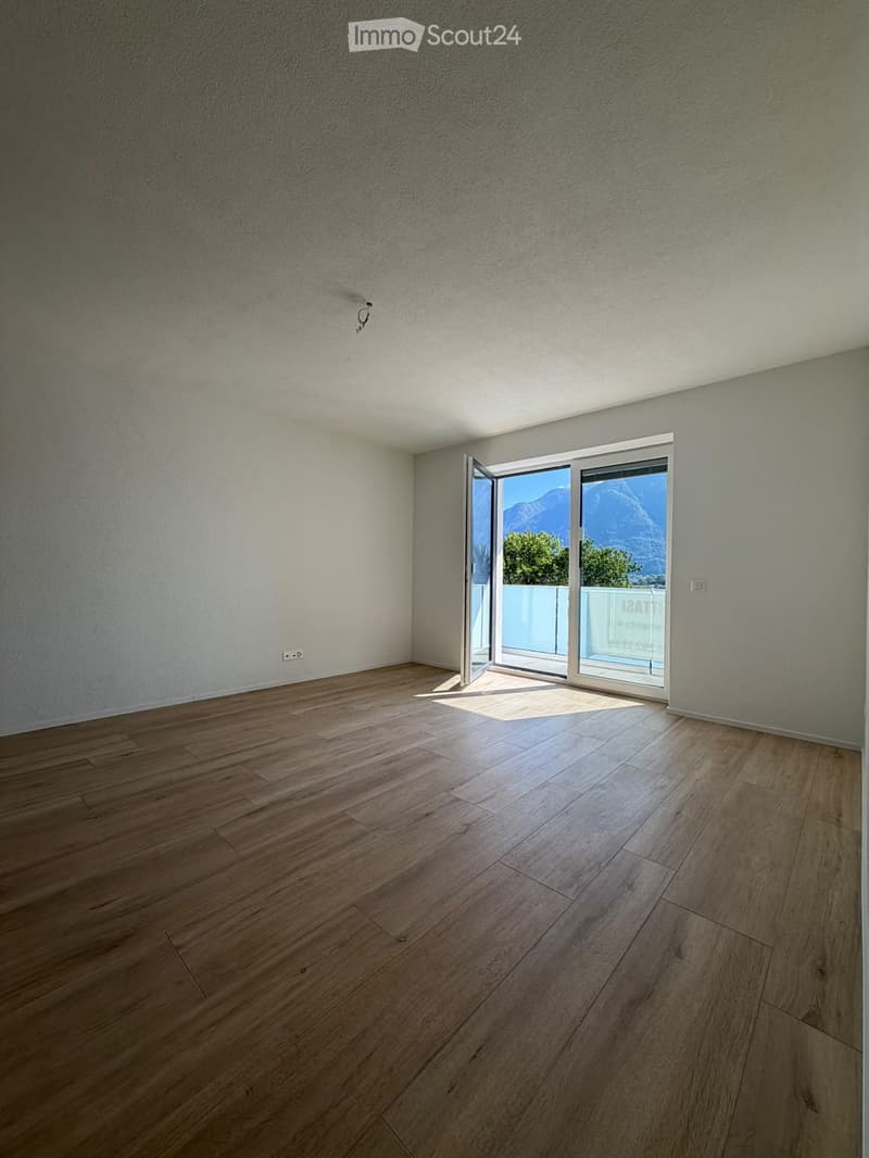 Empty room with wooden flooring, white walls, and large sliding glass doors leading to a balcony with a mountain view.
