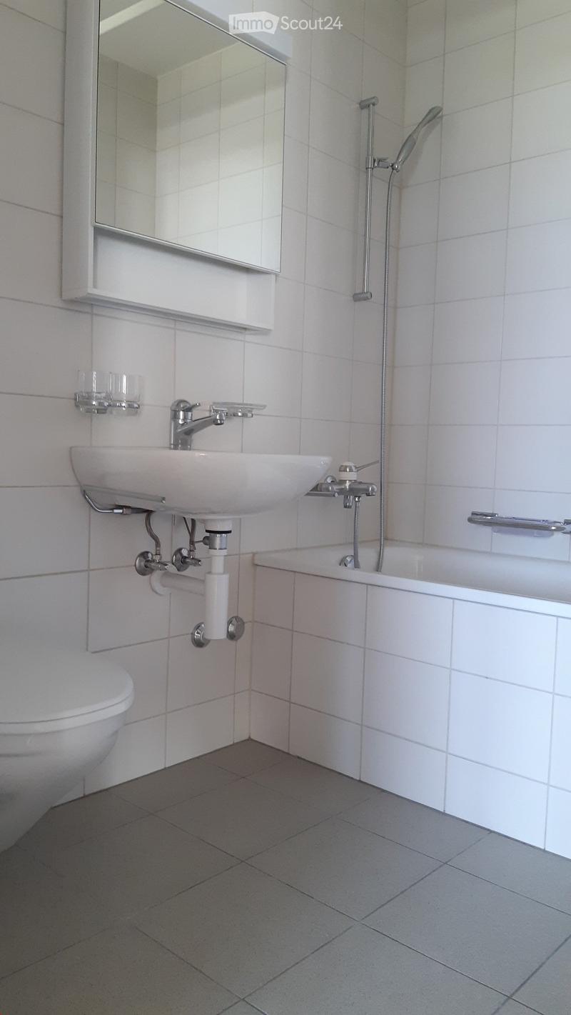 Modern bathroom with white tiles, a sink, mirror, bathtub, and toilet. Features a modern faucet and showerhead.