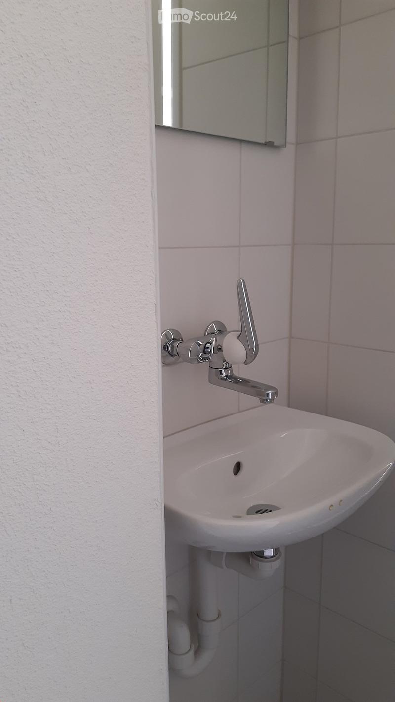 A small, modern bathroom sink with a chrome faucet mounted on light pink tiles, accompanied by a mirror above.