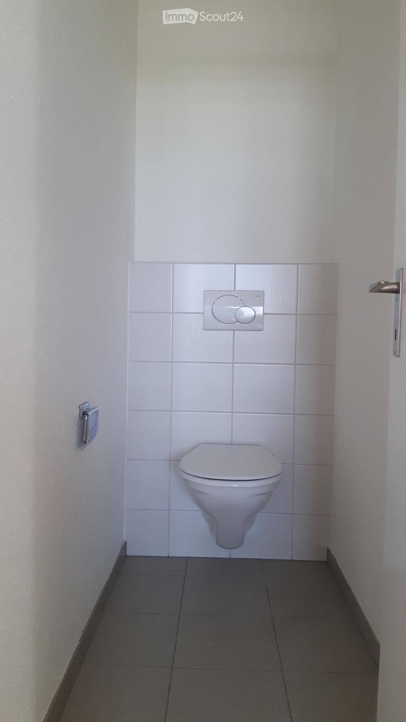 Modern bathroom with white tiled walls, a toilet, and a light switch on the wall.