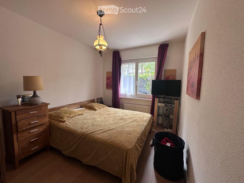 Cozy bedroom with a wooden bed, nightstand, lamp, television, and artwork on the walls.