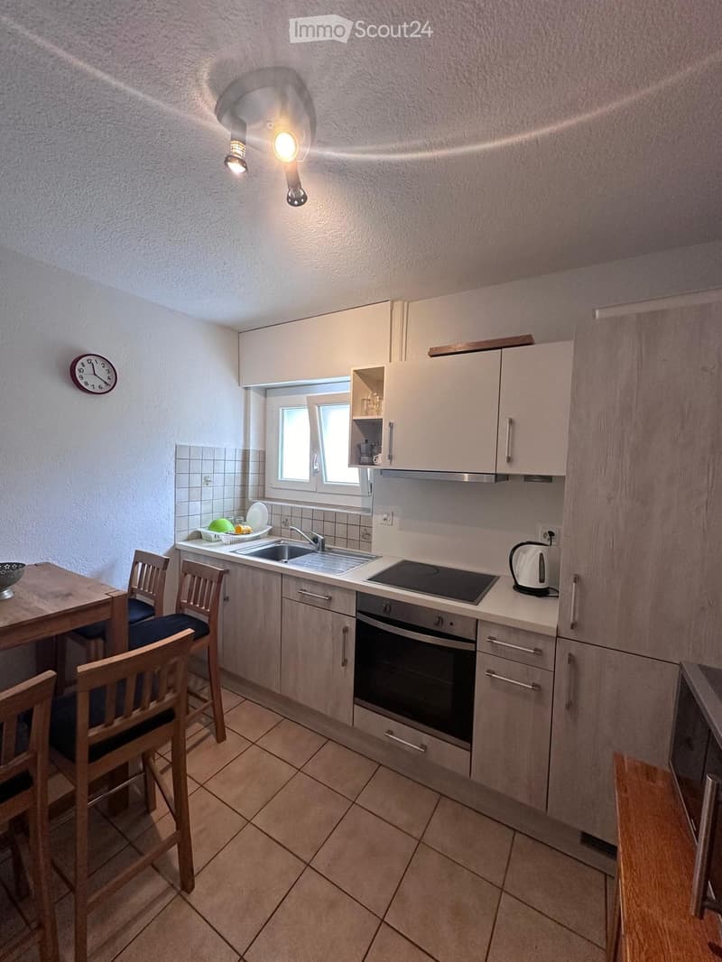 Modern kitchen with light-colored cabinets, a sink, an induction stove, an oven, and a small dining area with a table and chairs.