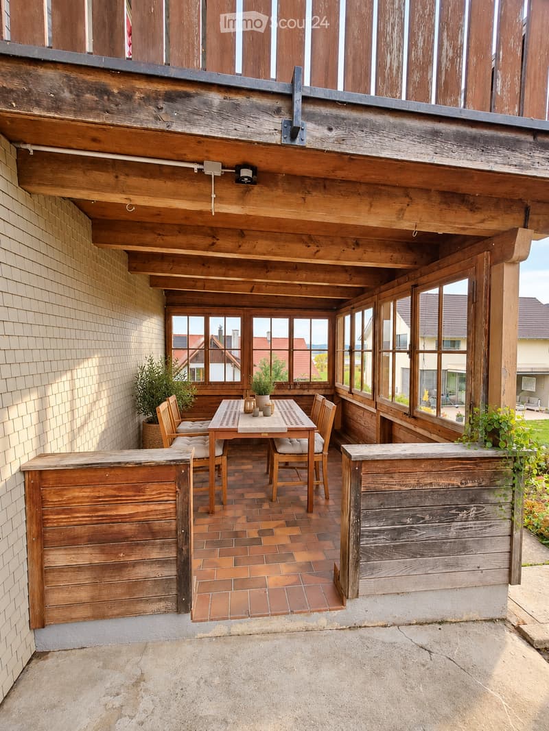 Wooden balcony with brick floor, table, chairs, bar counters, and potted plants.