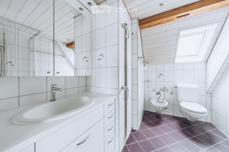 Modern bathroom with white tiles, a bathtub, toilet, bidet, and a large mirror above the sink.