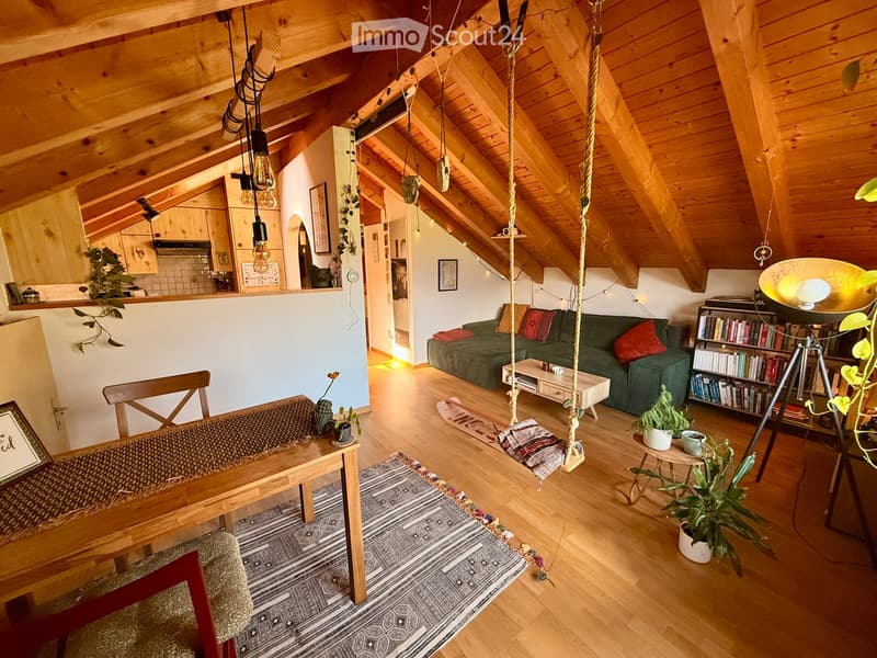 Cozy living room with exposed wooden beams, a green sofa, coffee table, bookcase, hanging swing, and potted plants.