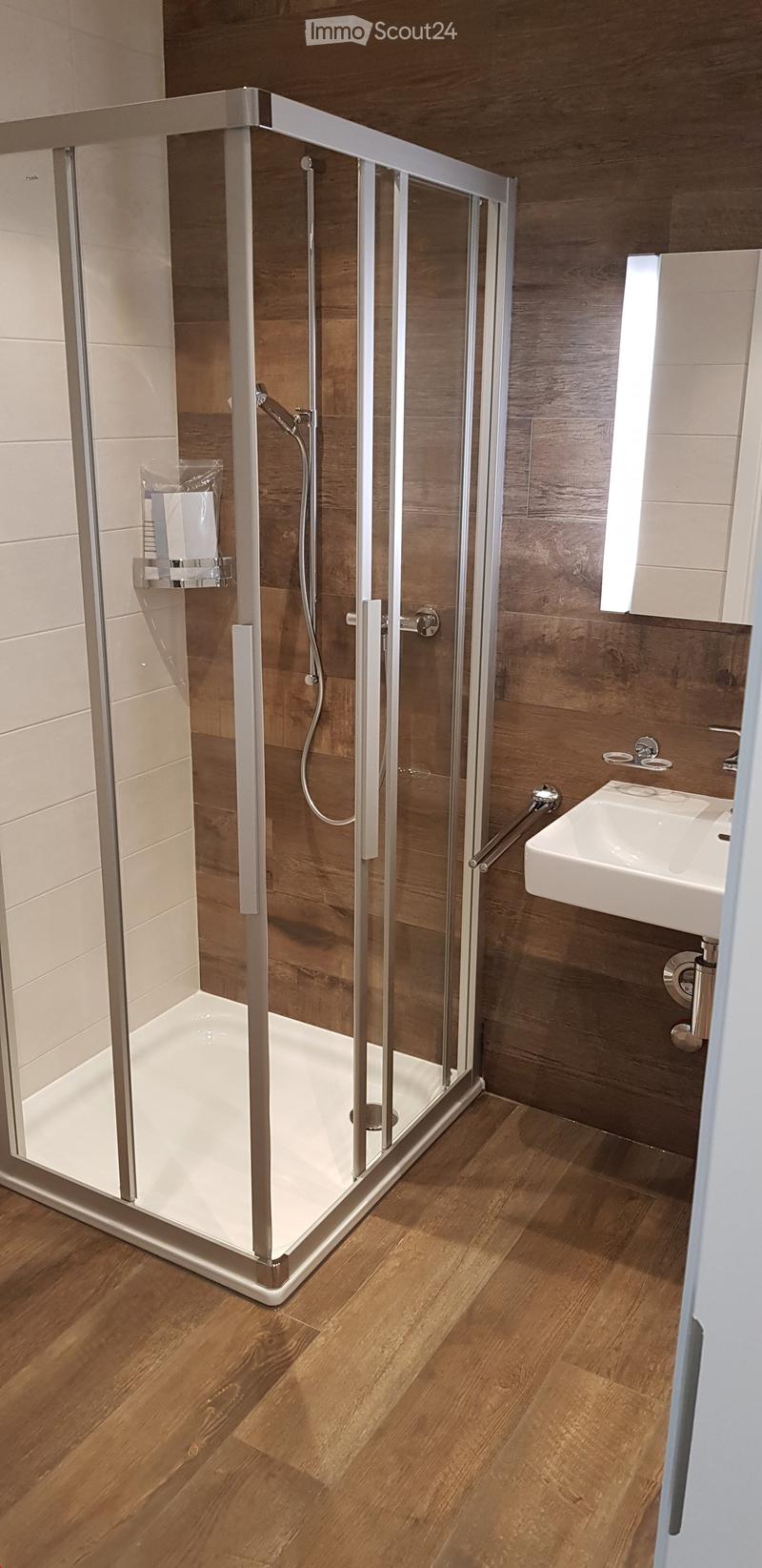 Modern bathroom with a glass-enclosed shower, wooden wall paneling, and a white sink with a chrome faucet.