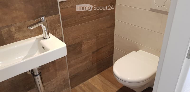 Modern bathroom with a white sink, chrome faucet, and white toilet. The walls are decorated with wood paneling and beige tiles.