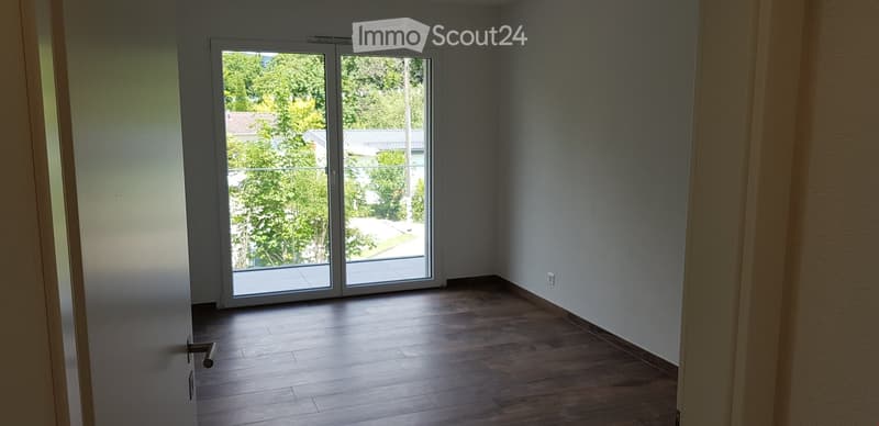Empty room with wooden flooring, large sliding glass doors leading to a balcony, and white walls.