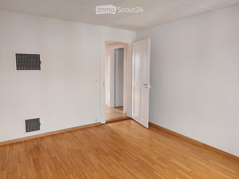 Empty room with light wooden flooring, white walls, and a partially open door leading to another room.