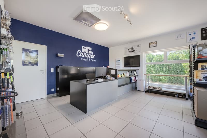 Modern reception area with a reception desk, screen, shelves with products, and a light fixture.